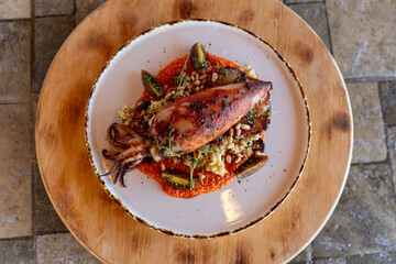 Grilled squid served on a bed of couscous with vegetables and sauce in a cozy dining setting