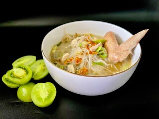 Soto ayam, a typical Indonesian dish, is served in a white bowl with an isolated black background