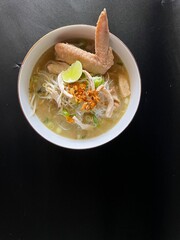 Soto ayam, a typical Indonesian dish, is served in a white bowl with an isolated black background