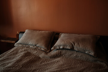 A neatly made bed with two pillows and patterned bedding in a room with a brown wall. Cozy and...