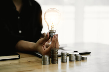 A person holds a glowing light bulb over stacked coins, symbolizing creativity, financial growth, investment strategy, creativity, success, and the connection between money and smart thinking.