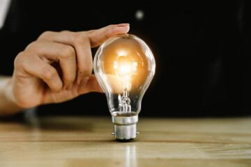 A person holds a glowing light bulb over stacked coins, symbolizing creativity, financial growth,...