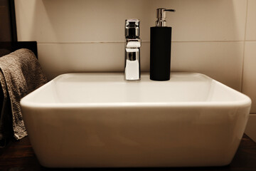 Modern white ceramic sink with chrome faucet and black soap dispenser. A soft towel hangs on the...
