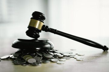 A gavel rests beside stacked coins and a balance scale, symbolizing justice, legal decisions,...