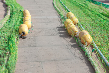 Fishing nets and buoys on a paved surface, ready for use. Green fishing nets with yellow floats lie...