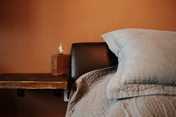 Close-up of a modern wooden bedside shelf with a minimalist lamp and gray bed linen in a cozy...