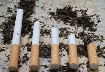 Five cigarettes of varying lengths are placed on map, surrounded by loose tobacco. arrangement suggests comparison or progression, with map providing textured background