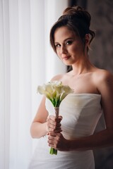 bride with a bouquet calla by windows in a hotel room.