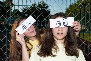Portrait of a two young women with a funny drawn paper eyes