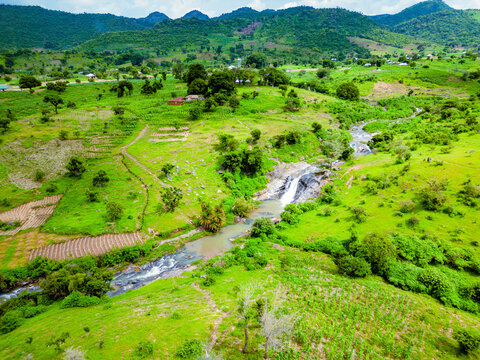 Aerial view of a vibrant landscape where a river cascades over rocks, carving through the green fields and lush vegetation, Maza village, Jos North, Nigeria.