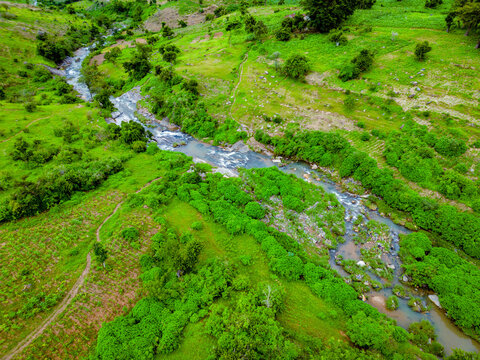 Aerial view of the vibrant river snaking through emerald hills, a tapestry of green contrasting with the water's cool serenity, Maza village, Jos North, Nigeria.