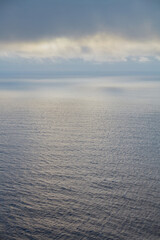 Vast ocean expanse under a cloudy sky with soft light reflecting on the rippled water surface,...