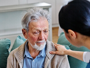 Doctor or nurse caregiver's hand giving support to sad lonely senior man at home or nursing home