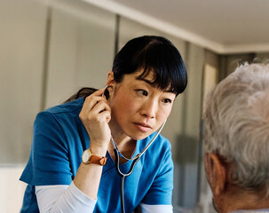 Doctor or nurse caregiver with senior man at home or nursing home using a stethoscope during an exam