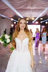 A bride with long blonde hair throws a bouquet to her bridesmaids at a banquet.