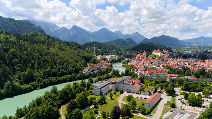 Aerial view of mountain town with red rooftops, green forest and turquoise river on sunny day under scenic sky