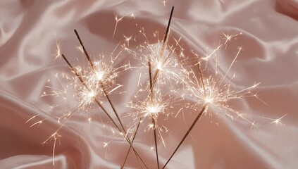 A set of sparklers burning on white fabric, against a soft pink background. 