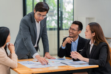 Group of happy Asian business people in suits brainstorming analyzing financial statistics. Meeting, discussion, corporate concept in office.