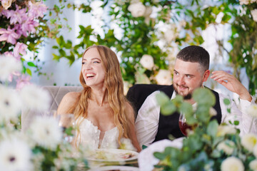 The bride and groom at the newlyweds' table, decorated with many flowers. 