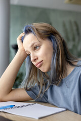 Focused female student sitting at desk with laptop, taking notes and studying online. Concept of digital learning, education, homework and academic growth.