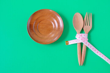 Measuring tape on a wood spoon and fork on color background.