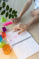 Two schoolgirls studying 3D geometric shapes during math class, drawing and discussing figures...
