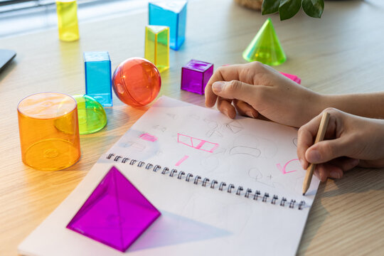 Two schoolgirls studying 3D geometric shapes during math class, drawing and discussing figures together as part of interactive STEM learning and teamwork activity in a modern classroom.