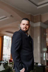 A serious, thoughtful man with a beard in a jacket in the lobby 