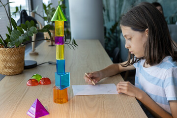 Teen girl studying geometric shapes at school desk, preparing for back to school season and exploring math concepts through colorful 3D figures during interactive learning activity in class.
