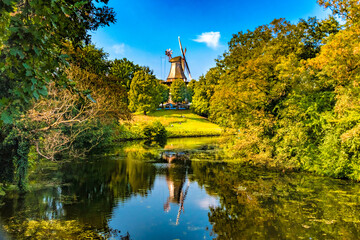 Lovely view of the famous windmill called "Mühle am Wall" or "Herdentorswallmühle" with a beautiful water reflection on a sunny day with a blue sky in the park called Wallanlagen.