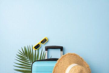 Top view of travel essentials including a suitcase, yellow sunglasses, and a straw hat
