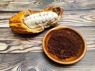 A ripe Cocoa or Theobroma cacao and a pile of chocolate powder in a wooden dish on a wooden table....