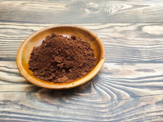 A closeup of a pile of chocolate powder in a wooden dish on a wooden table. Chocolate powder is a powder made from cocoa beans or Theobroma cacao that has been roasted, shelled, and ground.