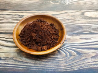 A closeup of a pile of chocolate powder in a wooden dish on a wooden table. Chocolate powder is a...