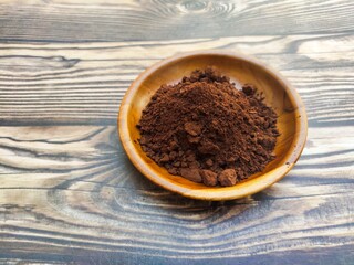 A closeup of a pile of chocolate powder in a wooden dish on a wooden table. Chocolate powder is a...