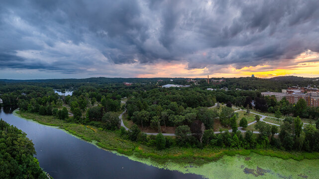 Aerial view of Moody Street and Charles River under a dramatic sky with sunset hues reflecting on the water, Waltham, Middlesex County, United States.