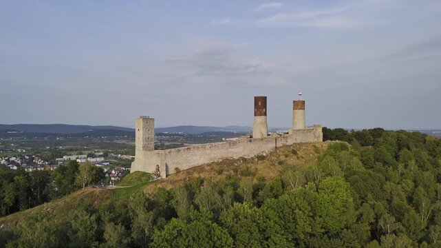 A stunning drone flight around the medieval Checiny Castle in Poland. The aerial view reveals the historic fortress, its stone walls, and the surrounding green hills.