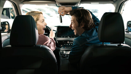 Young couple celebrating inside new car at dealership, showcasing excitement and joy during the car...