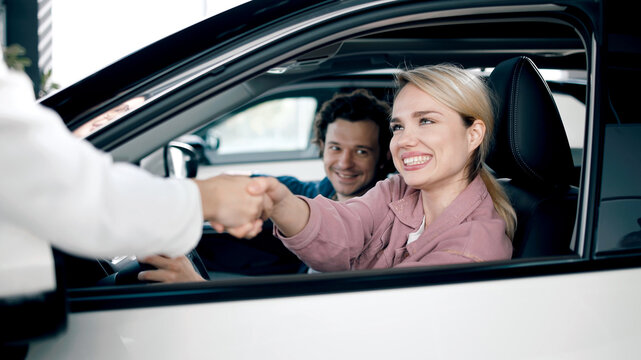 Happy couple shaking hands with car dealer inside showroom, celebrating successful purchase of new vehicle, showcasing customer satisfaction and excitement