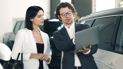 Car dealer presenting vehicle options to potential buyer in modern showroom, showcasing...