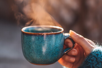 Steaming Coffee Cup: A hand gently cradles a beautiful blue ceramic mug of freshly brewed coffee, emanating a delicate wisp of steam, invoking the warmth and comfort of a cozy moment.