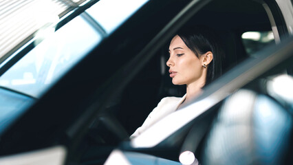 Woman sitting in car showroom, thoughtfully considering vehicle options, surrounded by modern cars...