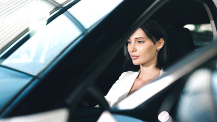 Woman in a car showroom is seated inside a modern vehicle, showcasing the interior design and...