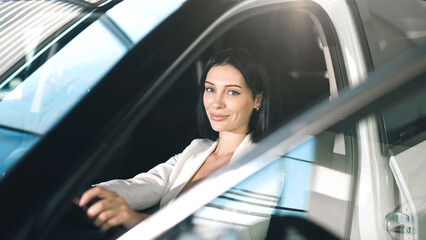 Confident woman in a car showroom, seated inside a modern vehicle, showcasing the excitement of...