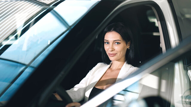 Confident woman in a car showroom, sitting inside a vehicle, showcasing the modern interior and bright ambiance of the dealership environment