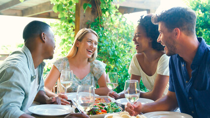 Group Of Smiling Multi-Cultural Friends Outdoors At Home Eating Meal And Drinking Wine Together