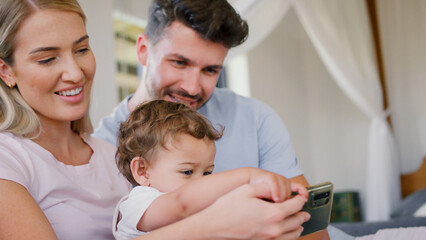 Family Sitting On Sofa At Home With Young Son Taking Selfie On Mobile Phone