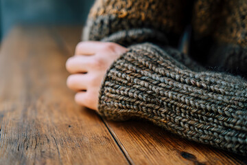Cozy Sweater and Wooden Table: A close-up view of a person's hand resting on a wooden table, wearing a warm and comfortable sweater, evoking feelings of warmth and relaxation.