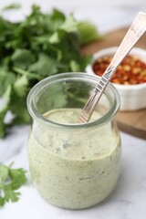 Tasty cilantro sauce and spoon in jar on light table, closeup