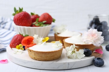 Delicious dessert. Tartlets with cream, berries and flowers on white tiled table, closeup